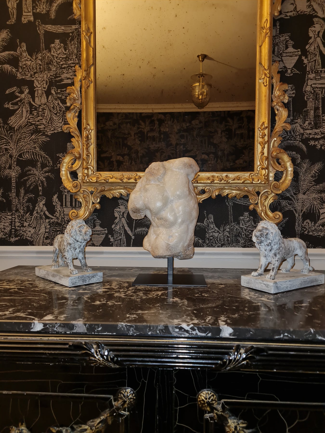 Marble sculpture of a torso and two dogs on a marble surface with an ornate gold mirror in the background.